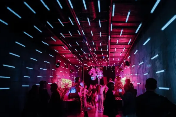 A crowded event space with vibrant pink and blue lighting and people dancing.