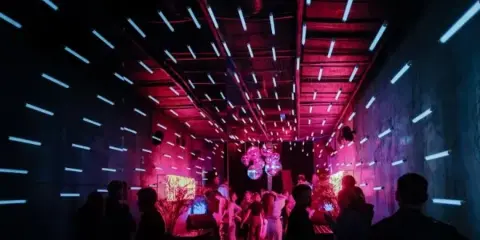 A crowded event space with vibrant pink and blue lighting and people dancing.