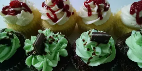 An assortment of gourmet cupcakes featuring white frosting with raspberry sauce and chocolate cupcakes with green frosting and chocolate garnish.