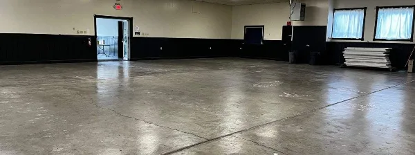Interior view of an empty banquet hall with a polished concrete floor and black wainscoting.