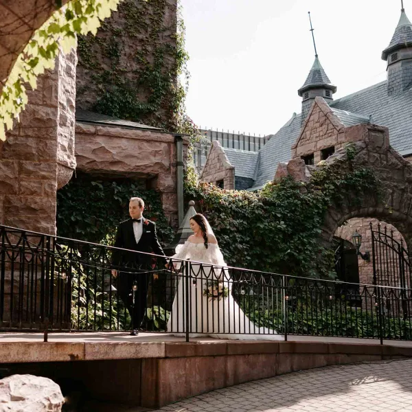 Bride and groom standing on a stone bridge in front of the castle-like Van Dusen Mansion