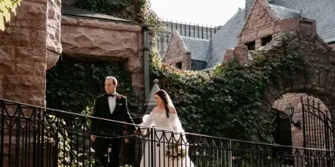 Bride and groom standing on a stone bridge in front of the castle-like Van Dusen Mansion