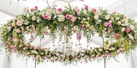 A lush, romantic floral installation with pink and white roses and greenery suspended from a chandelier in a white tent.