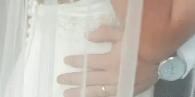 A close-up wedding photograph of a bride and groom embracing, with the groom's hand resting on the bride's waist, partially obscured by the bride's veil.