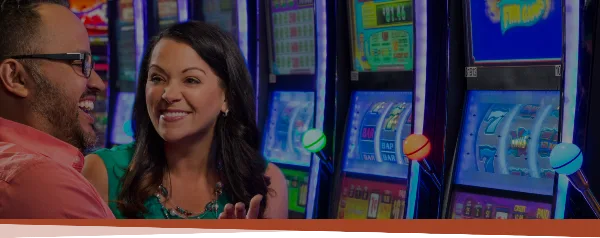 A couple smiling while standing in front of slot machines at a casino.