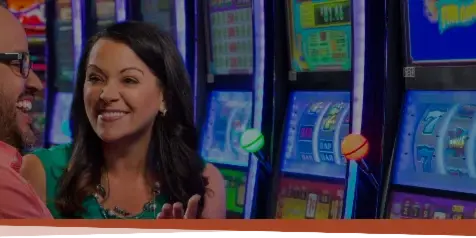 A couple smiling while standing in front of slot machines at a casino.
