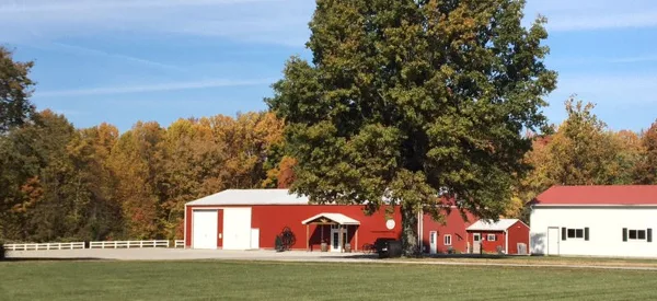 Exterior view of a red barn and white outbuildings at a country wedding venue with a large tree and grassy field.