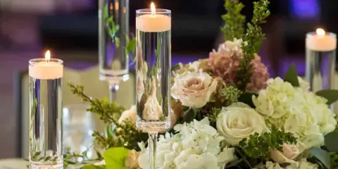 A close-up of a wedding reception floral centerpiece with white roses, hydrangeas, and tall glass pillar candles.
