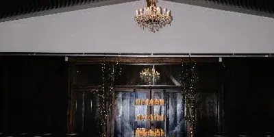 Interior view of a wedding venue featuring a long aisle lined with candles, rows of chairs, and crystal chandeliers hanging from a dark wooden ceiling.