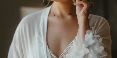 A smiling bride in a white robe with styled hair and makeup, looking down and to the side.