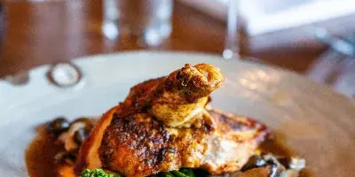 A plated dish of roasted chicken with broccolini and mushrooms served with a glass of red wine.