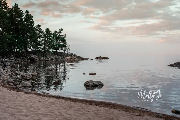 A serene Lake Superior shoreline at dusk with pine trees, rocks, and calm water, watermarked Molly Jo Photography.