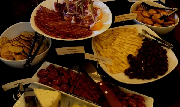 A catering table set with plates of sliced cured meats, cheese wedges, crackers, and olives.