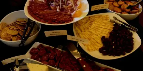 A catering table set with plates of sliced cured meats, cheese wedges, crackers, and olives.