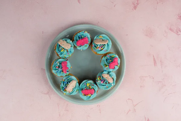 A plate of blue-frosted cupcakes topped with sprinkles and candy decorations on a pink marble surface.