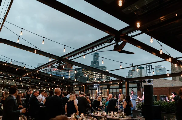 Guests at a rooftop event under a retractable glass ceiling with string lights and a view of the Chicago skyline.