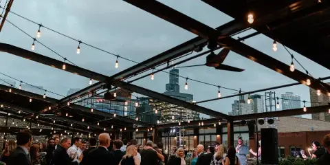 Guests at a rooftop event under a retractable glass ceiling with string lights and a view of the Chicago skyline.
