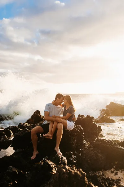 A cinematic photograph of a couple sitting on rocks by the ocean at sunset.