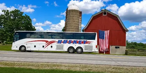 A white Huskey charter bus parked on a road in front of a red barn and silo.