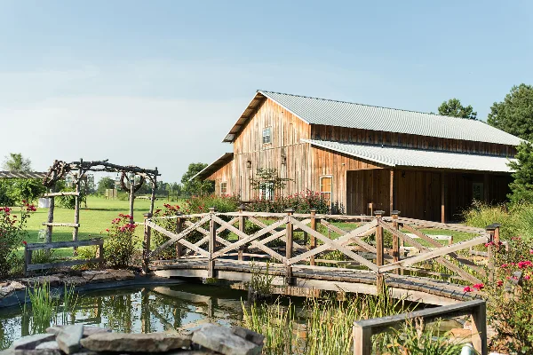 Exterior view of a wooden barn venue with a small bridge and garden.