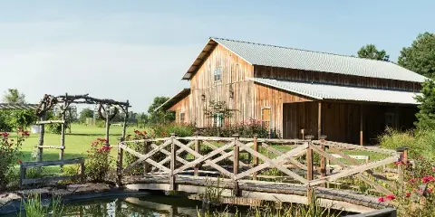 Exterior view of a wooden barn venue with a small bridge and garden.