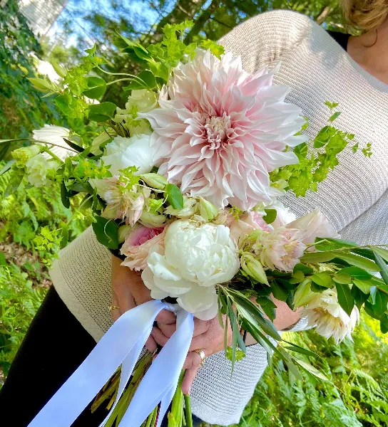 A person holding a large, lush floral bouquet with pink and white flowers and greenery.