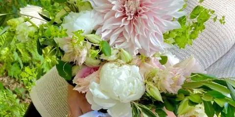 A person holding a large, lush floral bouquet with pink and white flowers and greenery.