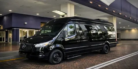 A black Mercedes-Benz Sprinter van parked at a covered drop-off area.