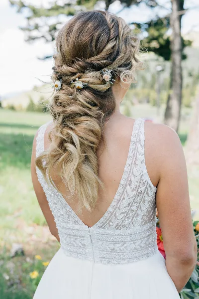 Bride from behind wearing a white lace dress with an elaborate braided updo hairstyle featuring small floral accents.