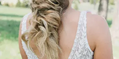 Bride from behind wearing a white lace dress with an elaborate braided updo hairstyle featuring small floral accents.