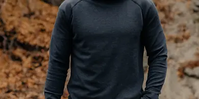 A man in a dark hoodie and jeans stands outdoors holding a professional camera.