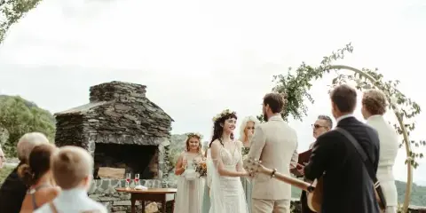 A bride and groom exchanging vows during an outdoor wedding ceremony on a stone terrace with a fireplace and mountain views.