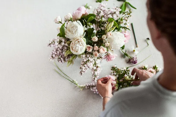 A florist arranging a bouquet of white and pink flowers on a white surface.