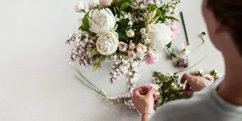 A florist arranging a bouquet of white and pink flowers on a white surface.