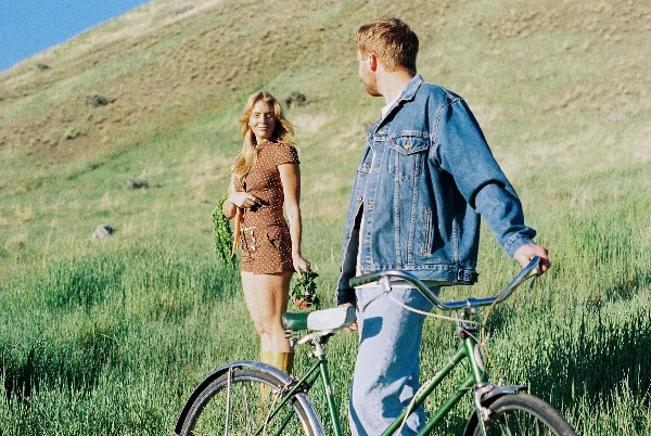 A couple standing in a grassy field with a bicycle, captured in a natural, documentary style.