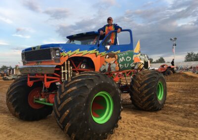 A colorful monster truck with a driver in the cab at an outdoor fairground event.