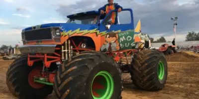 A colorful monster truck with a driver in the cab at an outdoor fairground event.