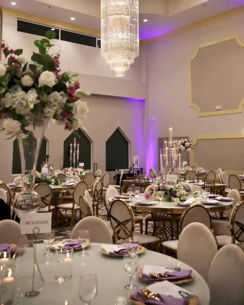 Interior view of a wedding reception hall featuring round tables, floral centerpieces, and a large crystal chandelier.