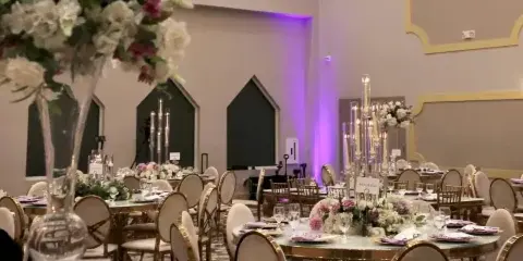 Interior view of a wedding reception hall featuring round tables, floral centerpieces, and a large crystal chandelier.