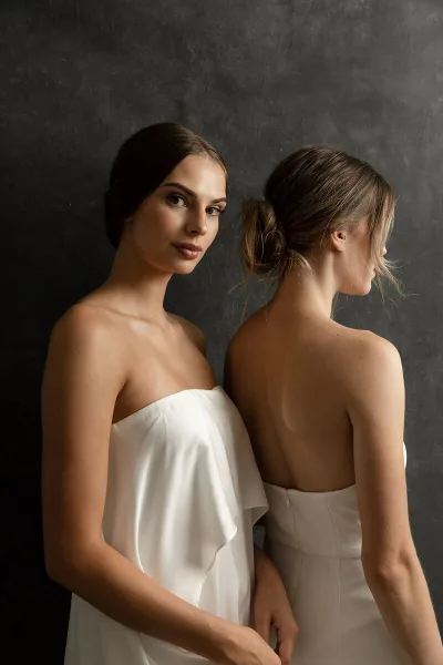 Two women in white dresses posing to display bridal hair and makeup styles