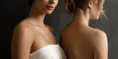 Two women in white dresses posing to display bridal hair and makeup styles