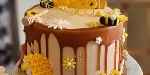 A custom decorated cake featuring honeycomb panels, fondant bees, and a honey dipper on a marble cake stand.