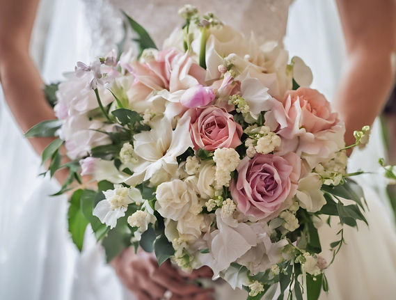 A bride in a white dress holding a large, custom wedding bouquet featuring pink and white roses, calla lilies, and greenery.