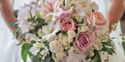 A bride in a white dress holding a large, custom wedding bouquet featuring pink and white roses, calla lilies, and greenery.