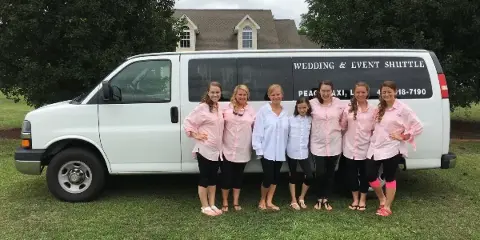 A group of women in matching pink shirts standing in front of a white Peach Taxi van labeled 'Wedding & Event Shuttle'.