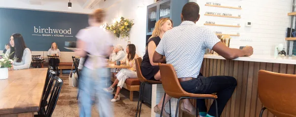 Interior view of the Birchwood Bakery + Kitchen dining room with customers seated at tables and a branded wall sign.