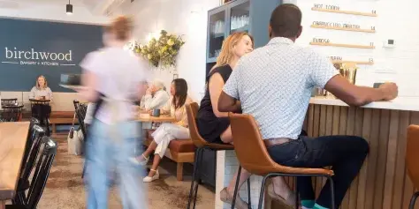 Interior view of the Birchwood Bakery + Kitchen dining room with customers seated at tables and a branded wall sign.
