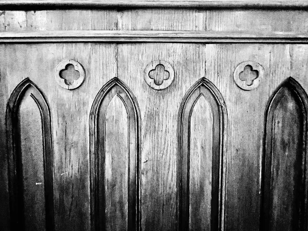 Black and white photograph of a wooden panel with Gothic arches and quatrefoil cutouts.