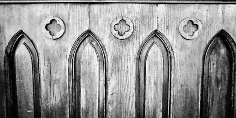 Black and white photograph of a wooden panel with Gothic arches and quatrefoil cutouts.
