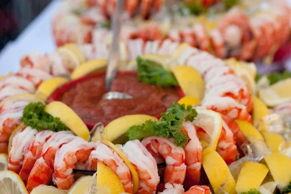 A close-up of a shrimp cocktail platter garnished with lemon wedges and parsley, served with a dipping sauce.